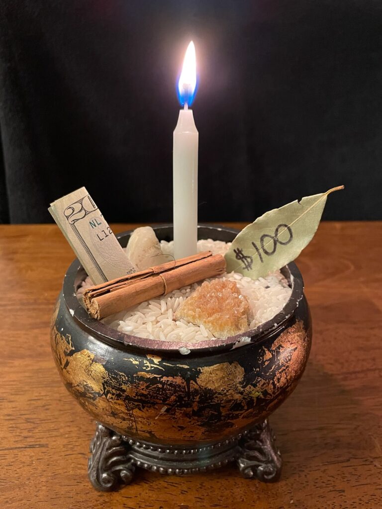a bowl filled with rice with a white candle, a bay leaf with $100 written on it, and a twenty-dollar bill sticking out of the rice. laying on top of the rice it two crystals and a cinnamon stick. 